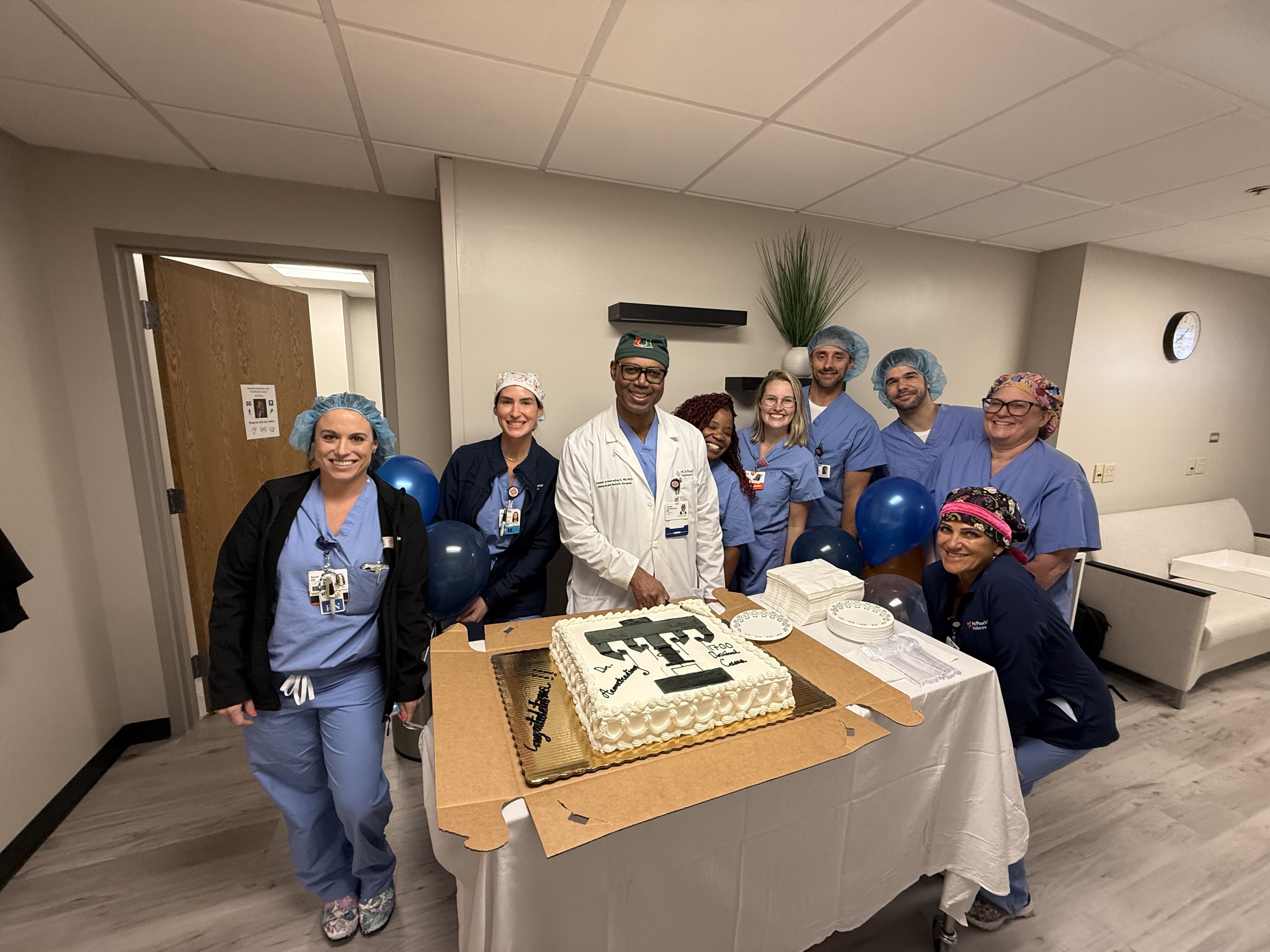 Northside hospital team members and Dr. Joseph Armotrading pose with cake decorated with image of robotic surgery device.