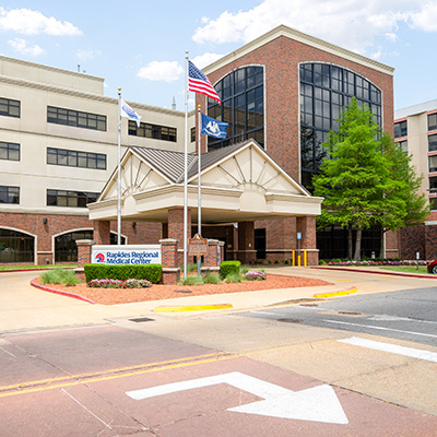 Exterior view of the Rapides Regional Medical Center building with hospital sign behind a driveway with American flag flying from a flagpole. 