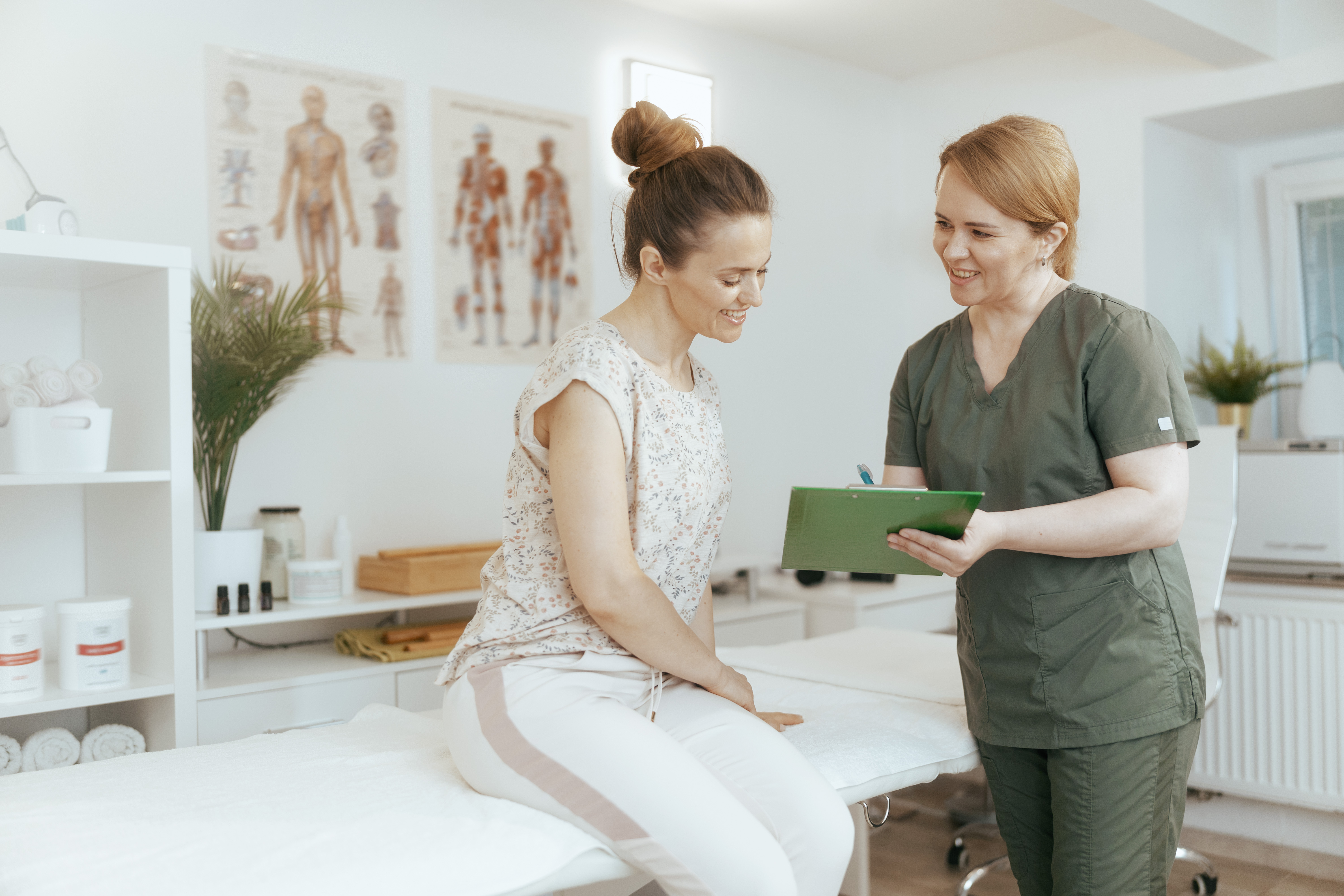 Massage therapist smiling with her patient, while writing on a clipboard.
