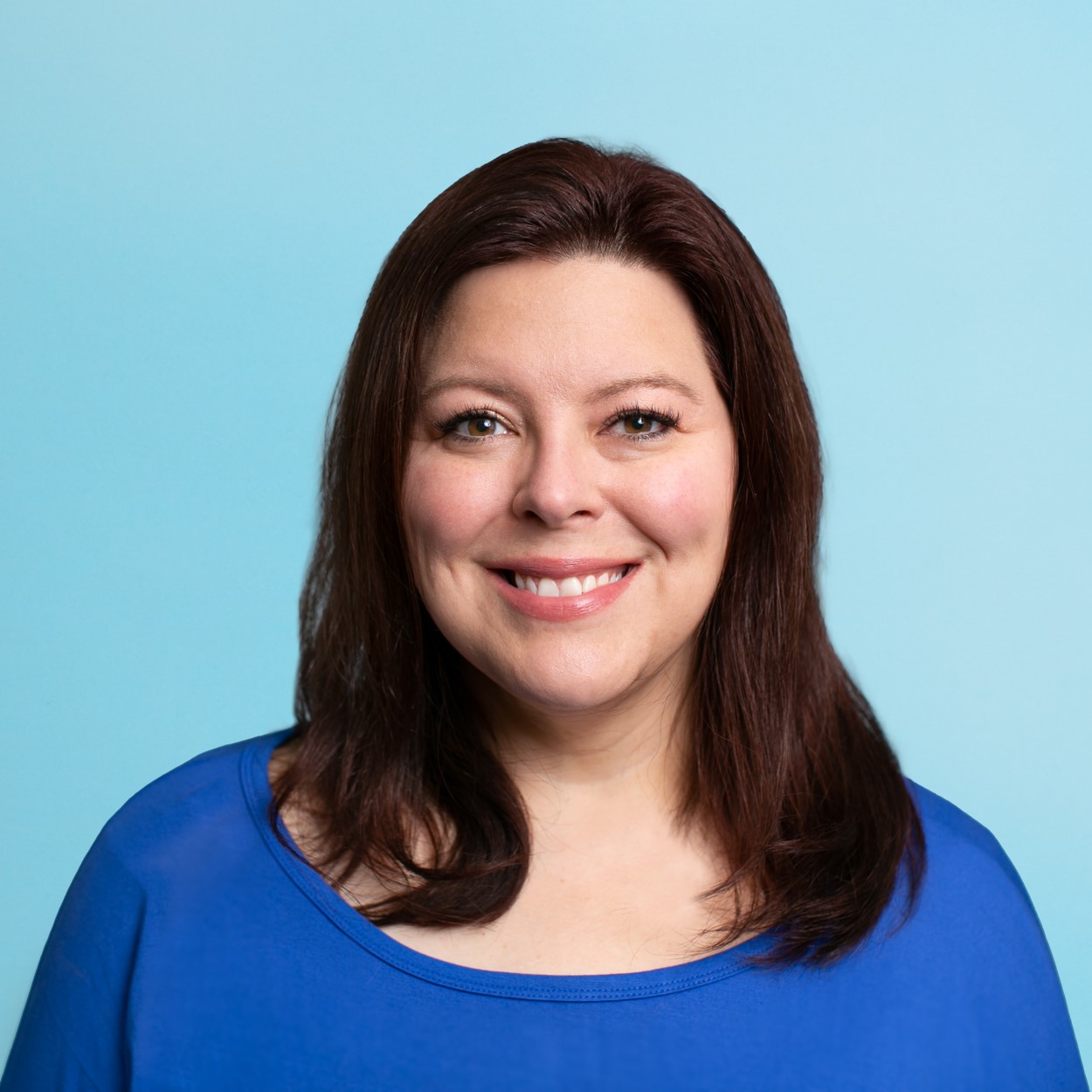 Melissa smiles for the camera, wearing a blue top against a cerulean background.