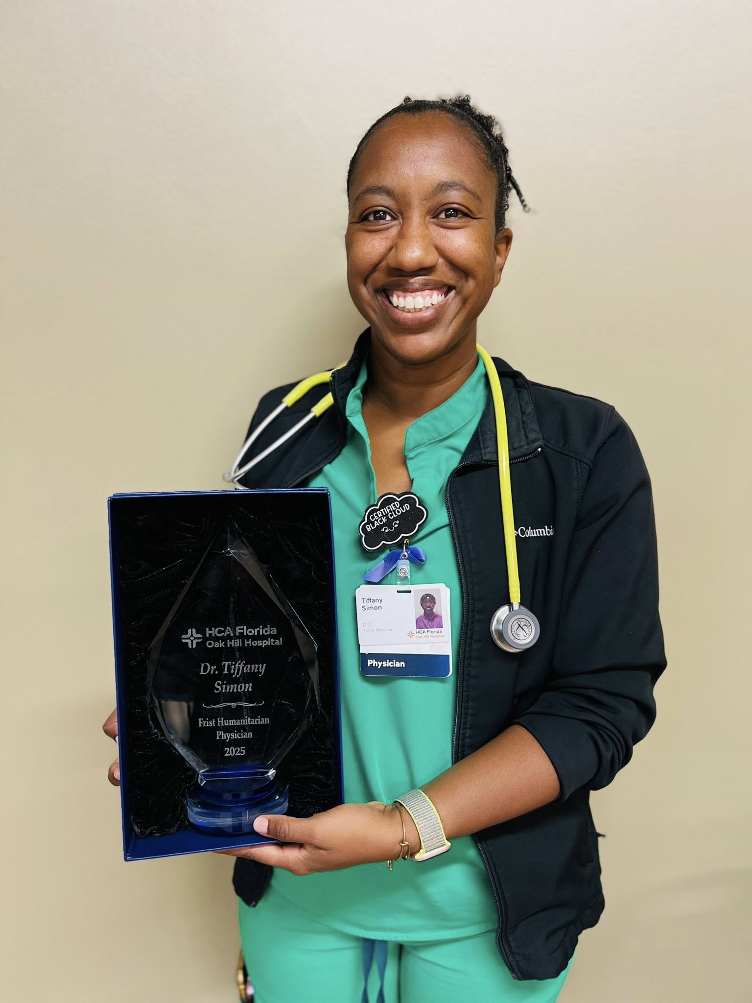 Dr Simon posing and smiling for a picture, holding Frist Humanitarian and Excellence in Nursing Award Certificate.