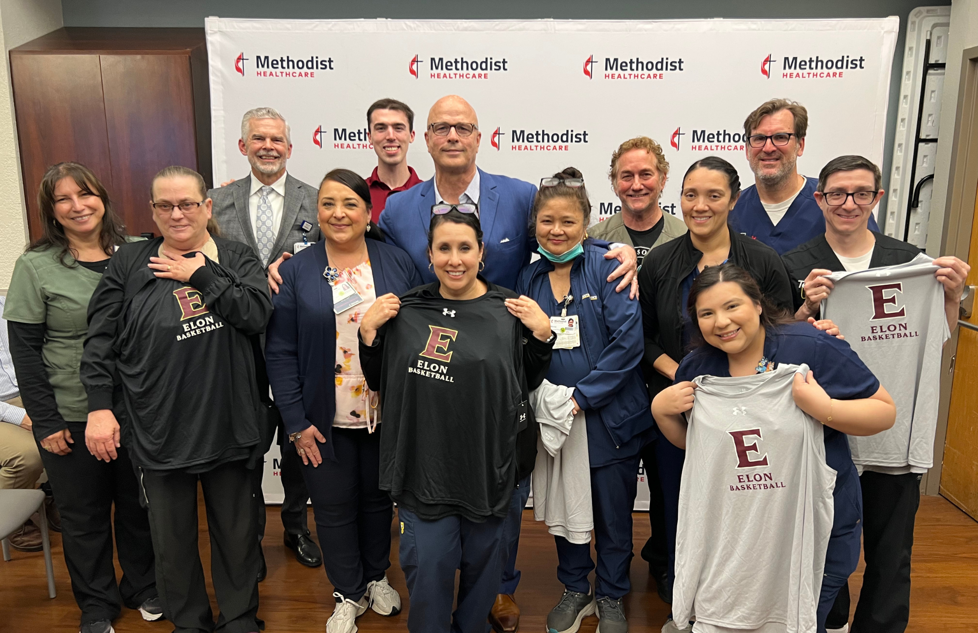 Greg Herenda posing for a photo holding jerseys together with the Methodist Hospital Metropolitan staff.