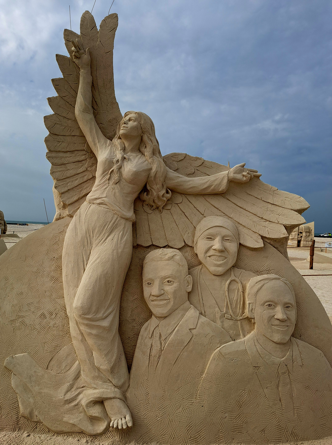 Sand sculpture with an angel and three faces of physicians