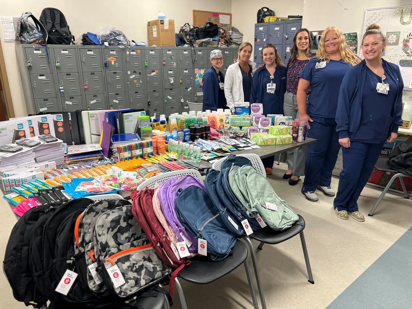 Hospital nurses and leadership smile with nonprofit leaders next to a table full of supplies.