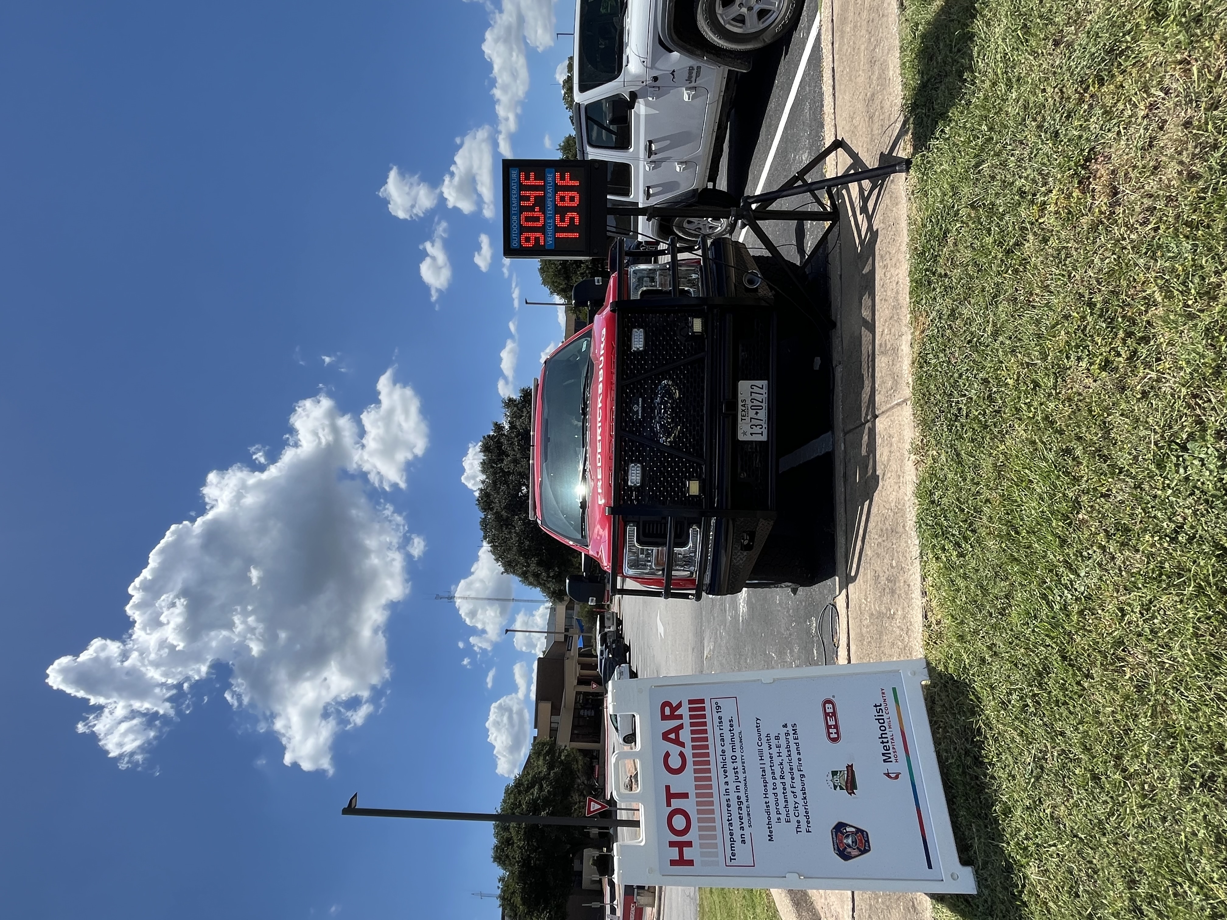 outdoor photo of truck in parking lot with digital sign measuring temperature outside and inside the; "outdoor temperature: 90.4 degrees Fahrenheit" "indoor temperature: 158 degrees Fahrenheit"; also featuring "hot car" sign with safety information