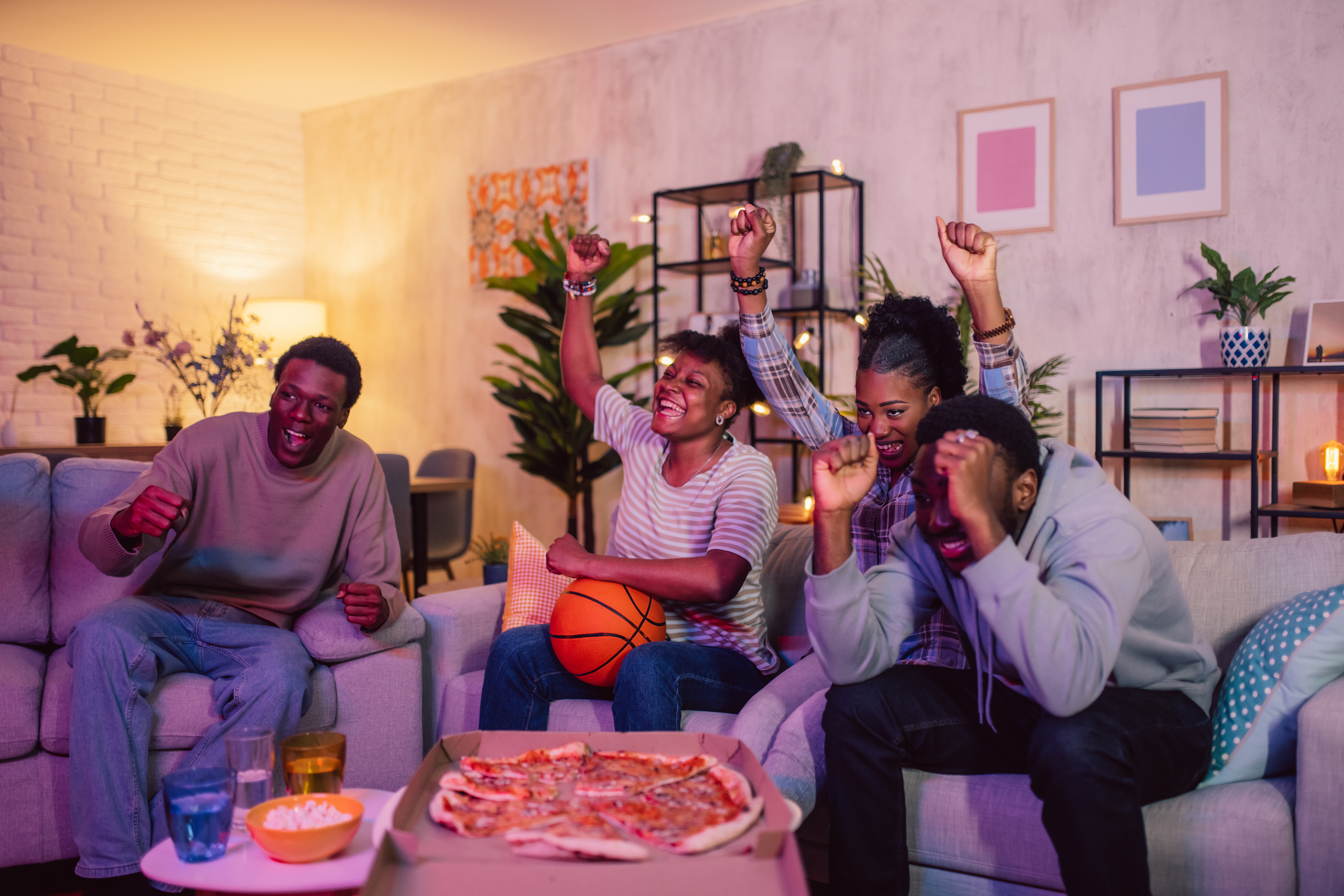 Friends eating pizza while watching a basketball game in a living room.