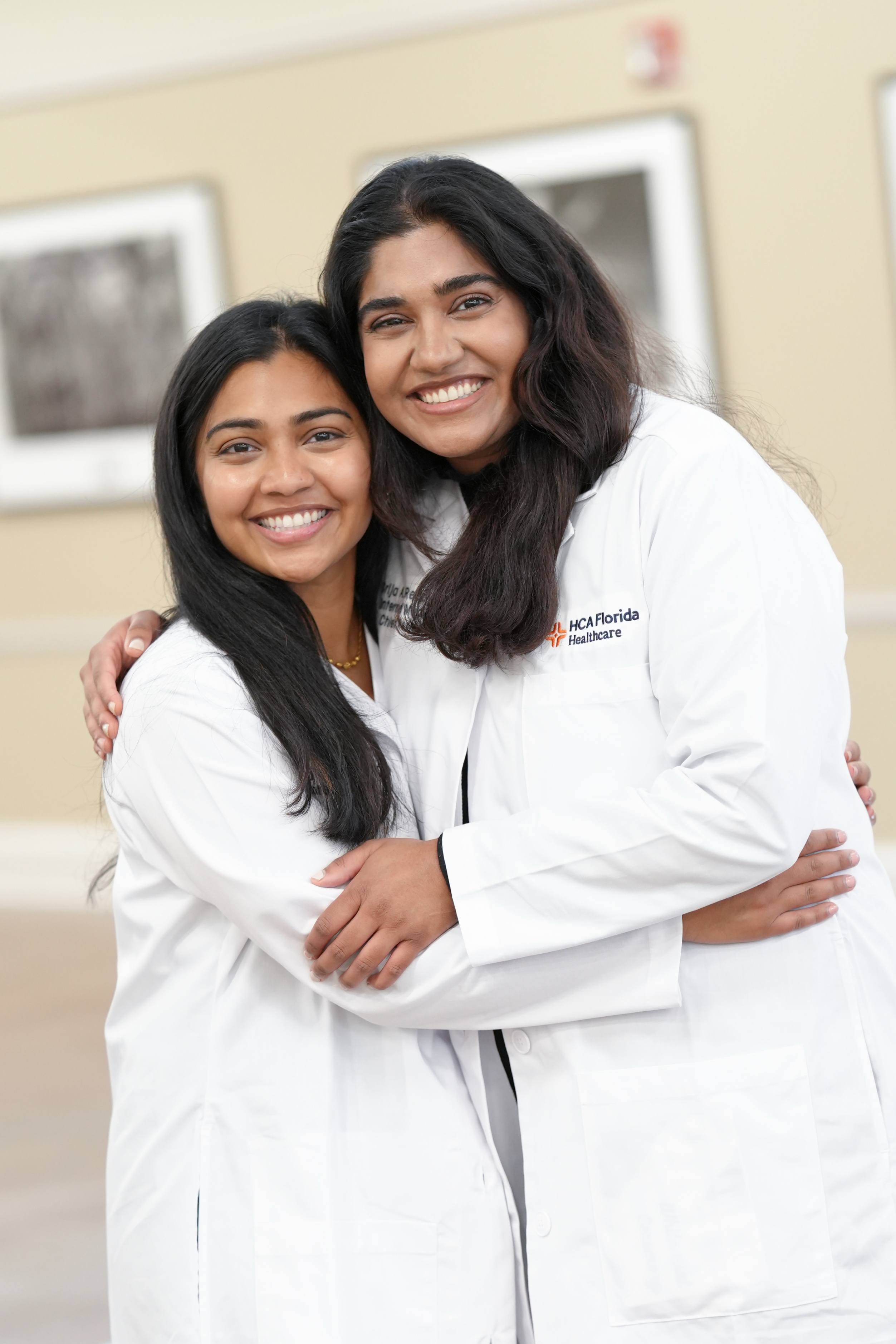 Doctor sisters Srija Reddy, MD and Sriya Reddy, DO hugging in white coats