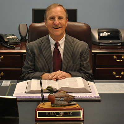 Pastor Billy Miller smiles while seated at his desk, with a Bible open in front of him.