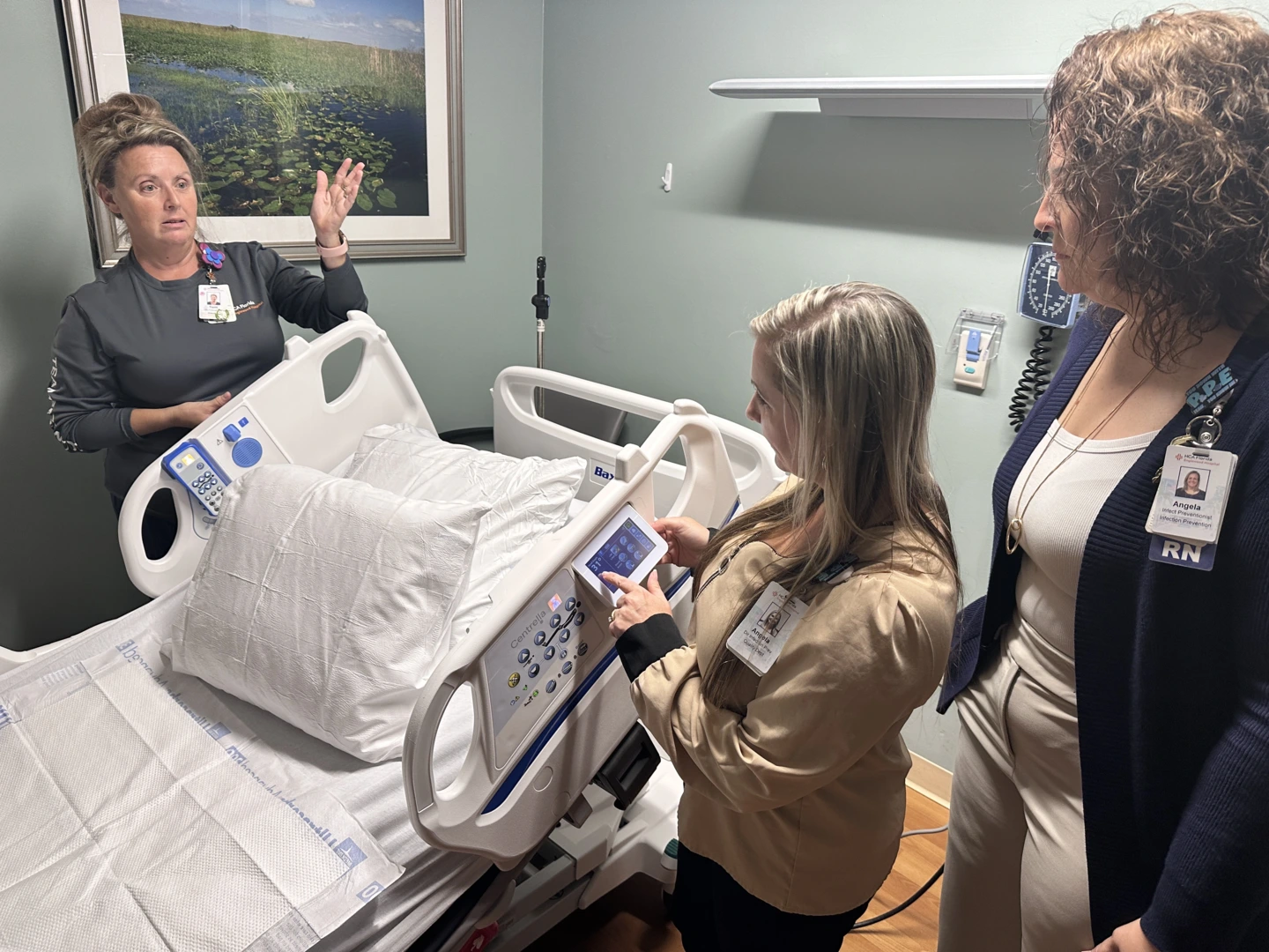 Two nurses and an educator talk next to a patient bed.