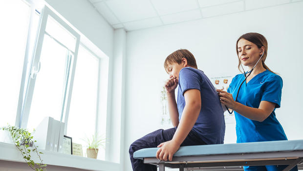 Child coughing on doctor's table while being checked by doctor with stethoscope