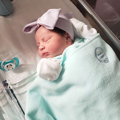 Newborn baby, Ilyana Sandoval, wearing a cotton head bow and mittens.