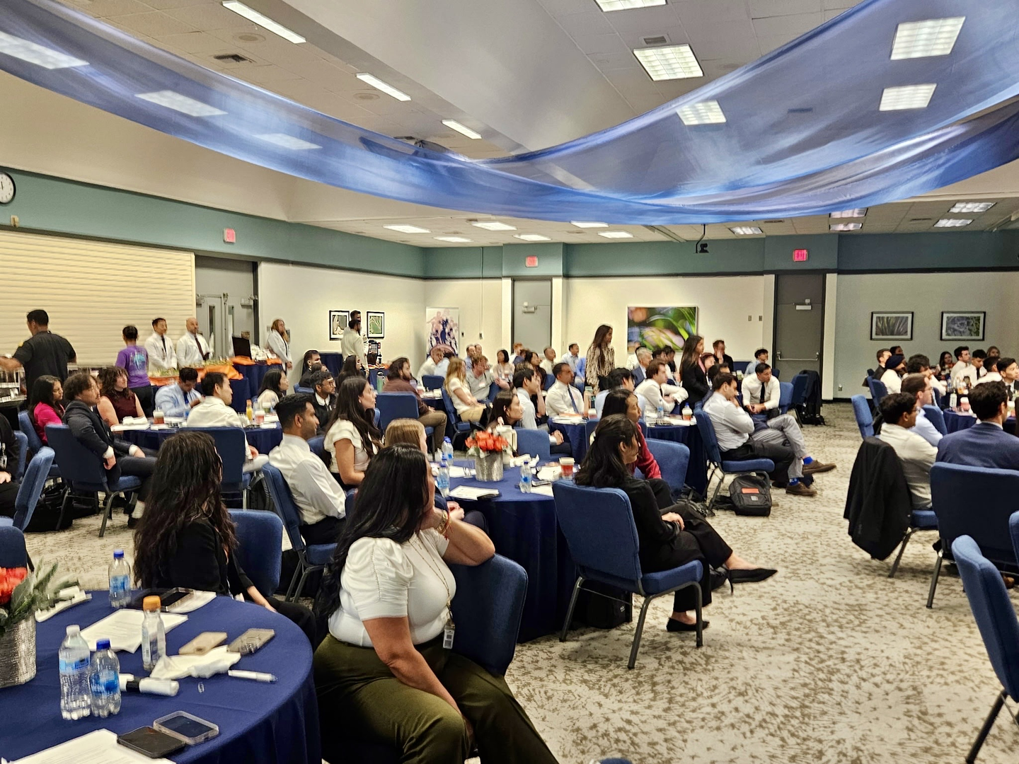 Photo showing of a group of man and woman, sitting during the welcoming ceremony for the new residents and fellows of Riverside Community Hospital.