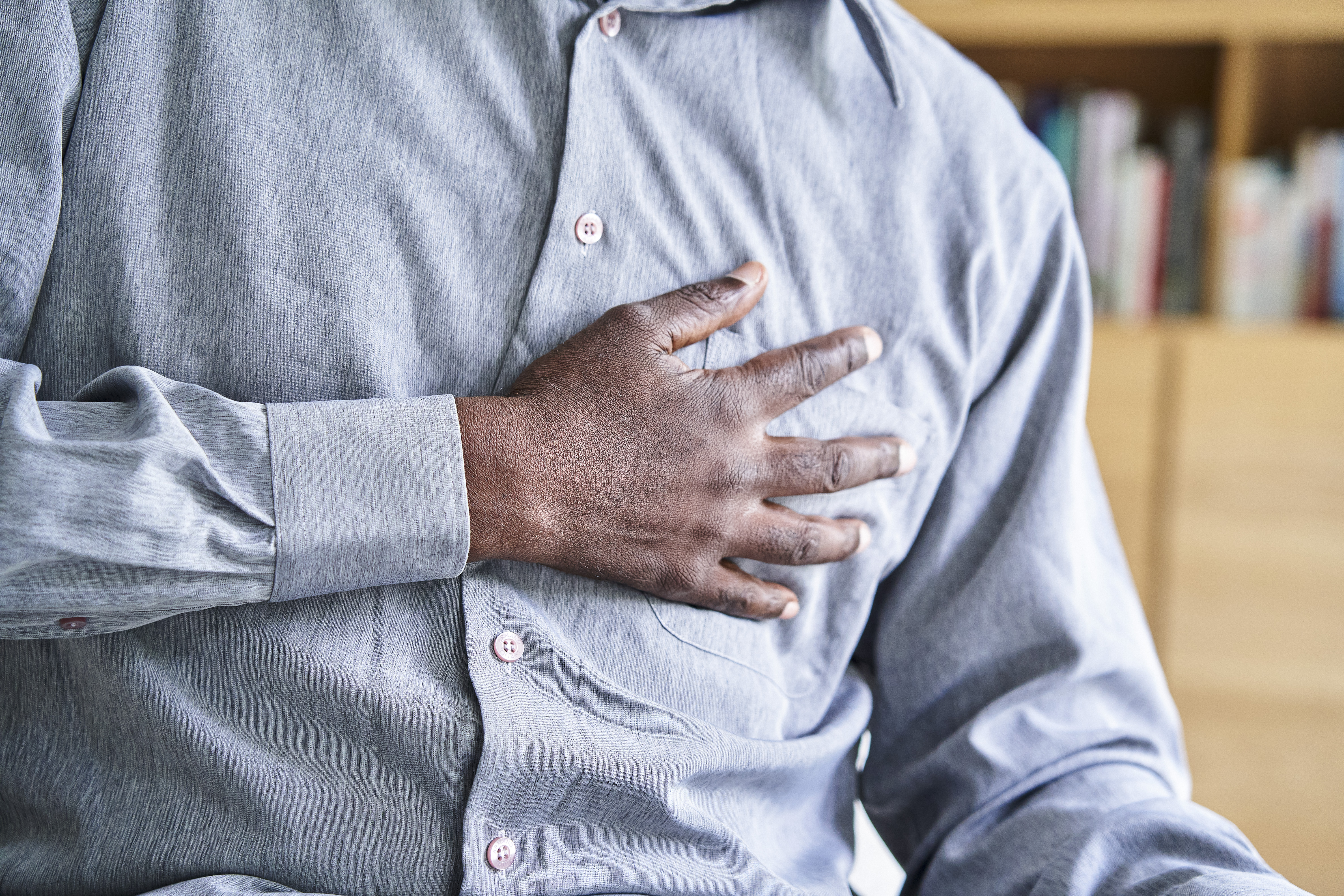 A man clutches his chest with his hand, indicating chest pain.