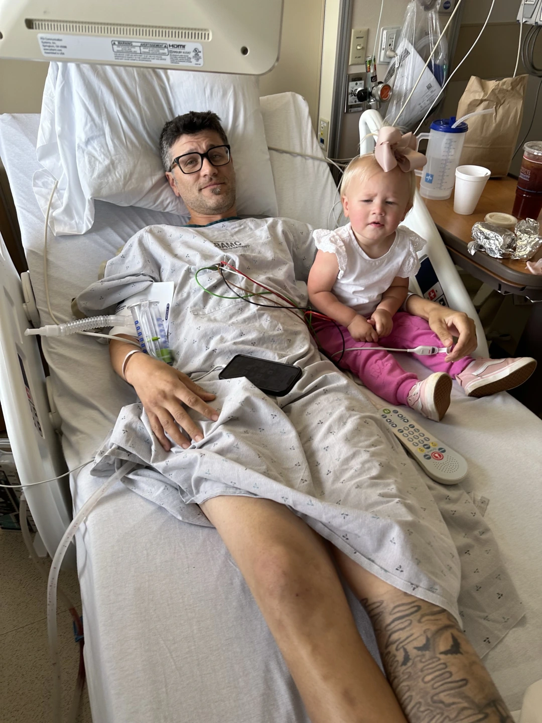 Kody lays in bed, his daughter sits next to him