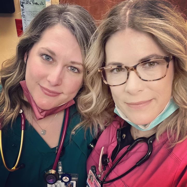 Two women standing together in a pink scrub top and glasses and one in a teal scrub top.