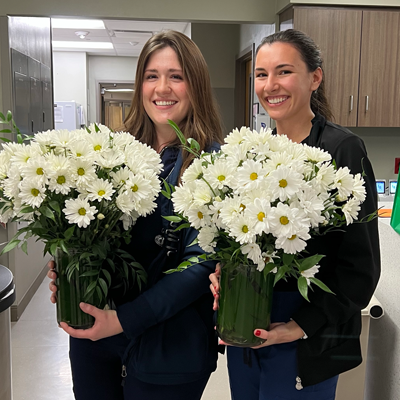 Shannon Irwin and Lauren Demarco hold daisy bouquets.