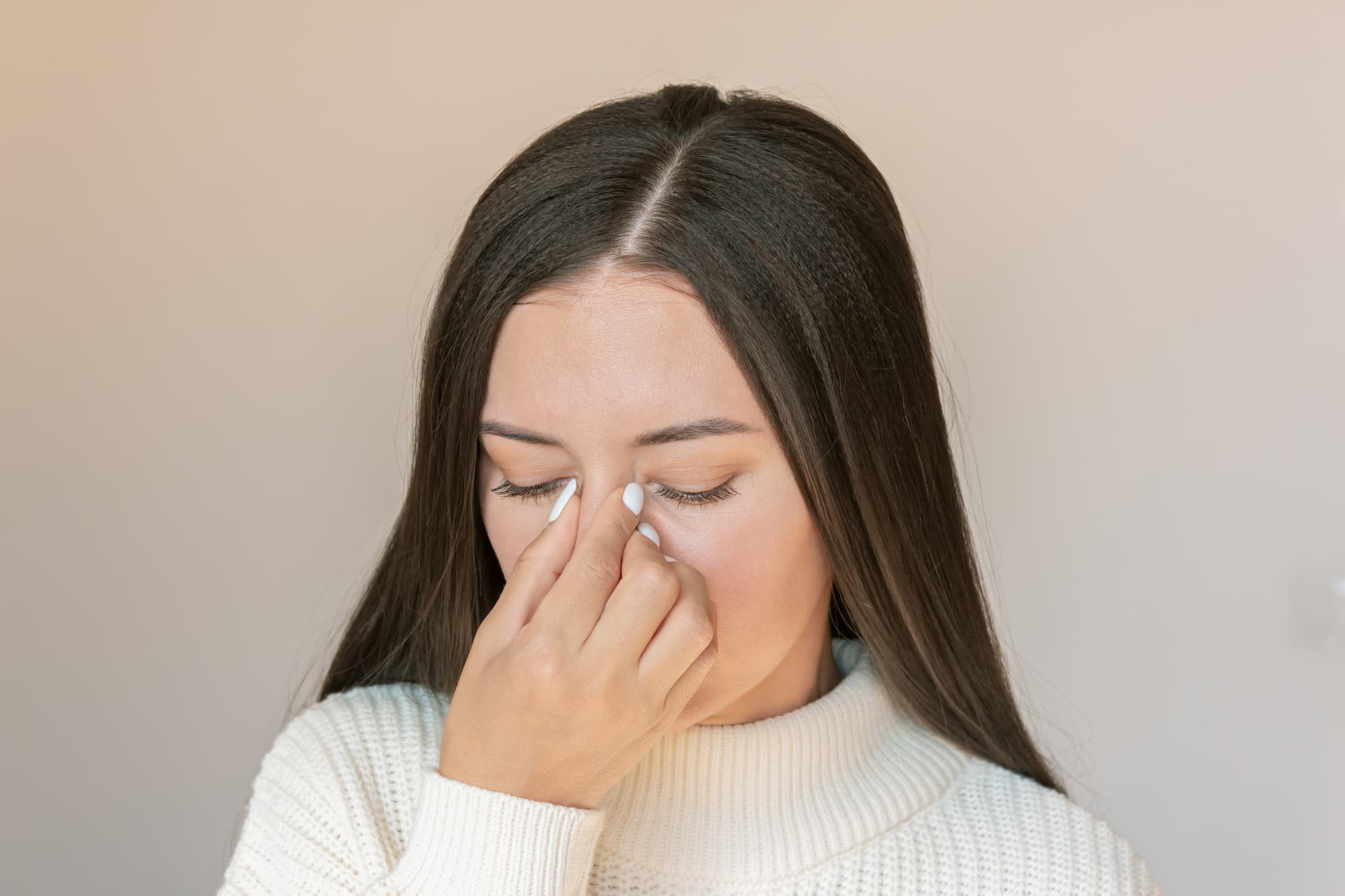 A woman holds the bridge of her nose between her thumb and forefinger with her eyes closed.