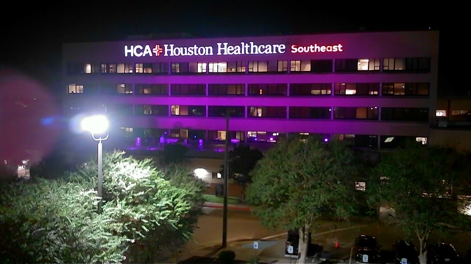 The facade of HCA Houston Healthcare Southeast lit up purple at night