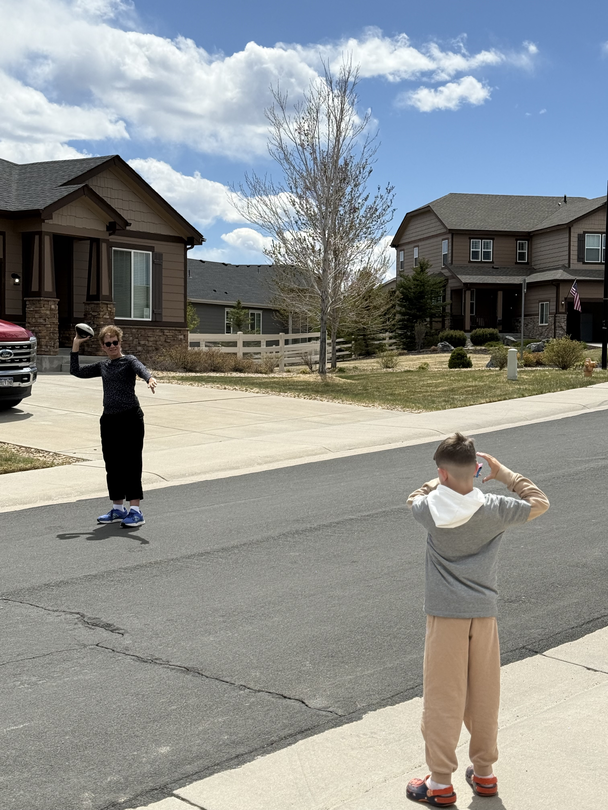 Diane throwing a football with her grandson in street.
