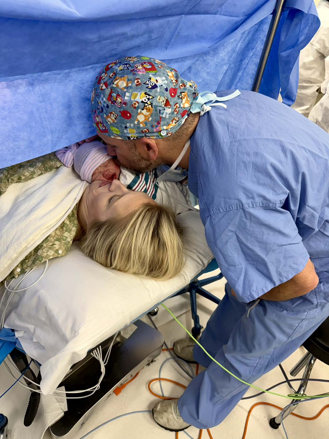 Danielle after giving delivery in the hospital room with her husband, who is also a CRNA member at the hospital - both kissing their newborn baby girl.