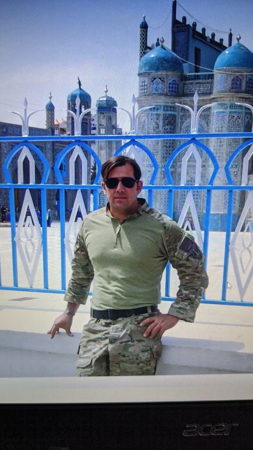 Ed Prescott stands in front of a blue and white tile building while on duty during his time as a Green Beret.
