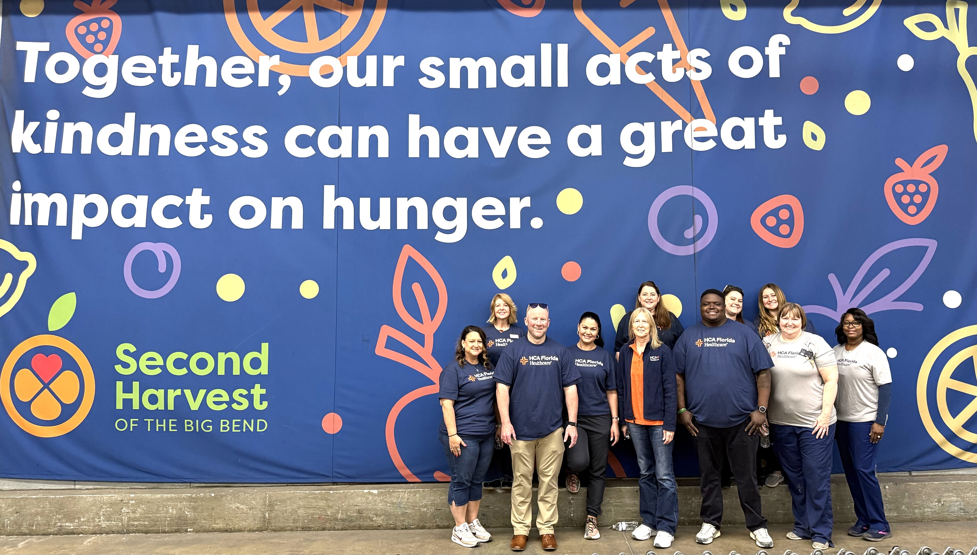 Group of people standing in front of sign that reads, Together, our small acts of kindness can have a great impact on hunger. Second Harvest of the Big Bend."