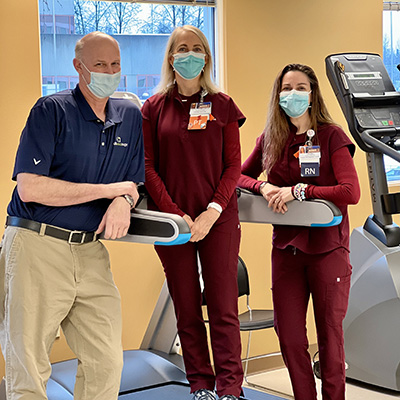 Jim leaning on a treadmill standing next to two nurses.