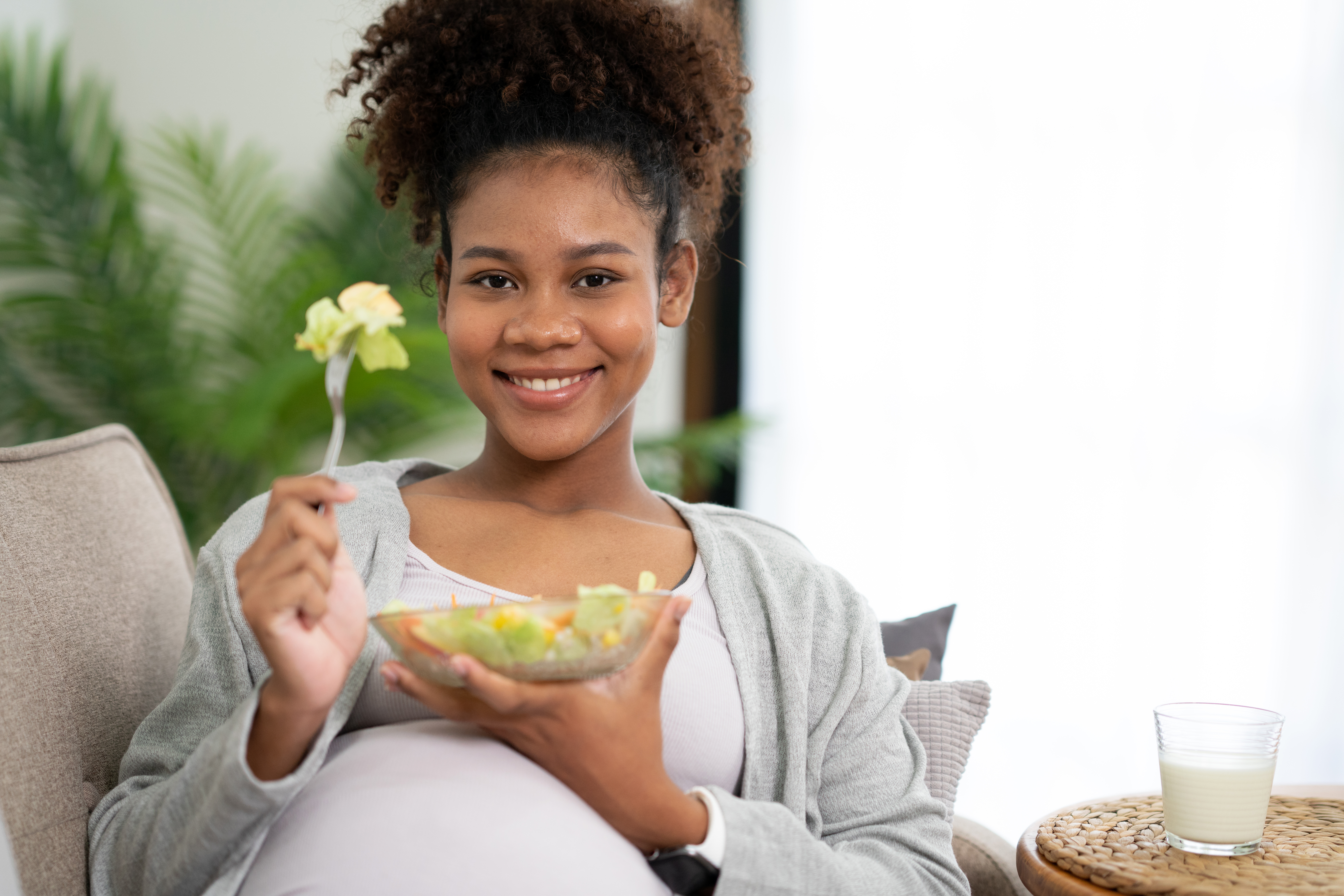 An expectant mom smiles while eating a salad