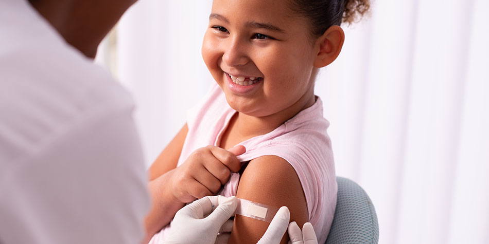 Doctor placing a bandage on a young smiling girl after she received a vaccine shot.