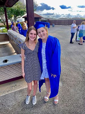Cancer Survivor Kate Hardaway in a graduation robe and cap standing next to her friend.