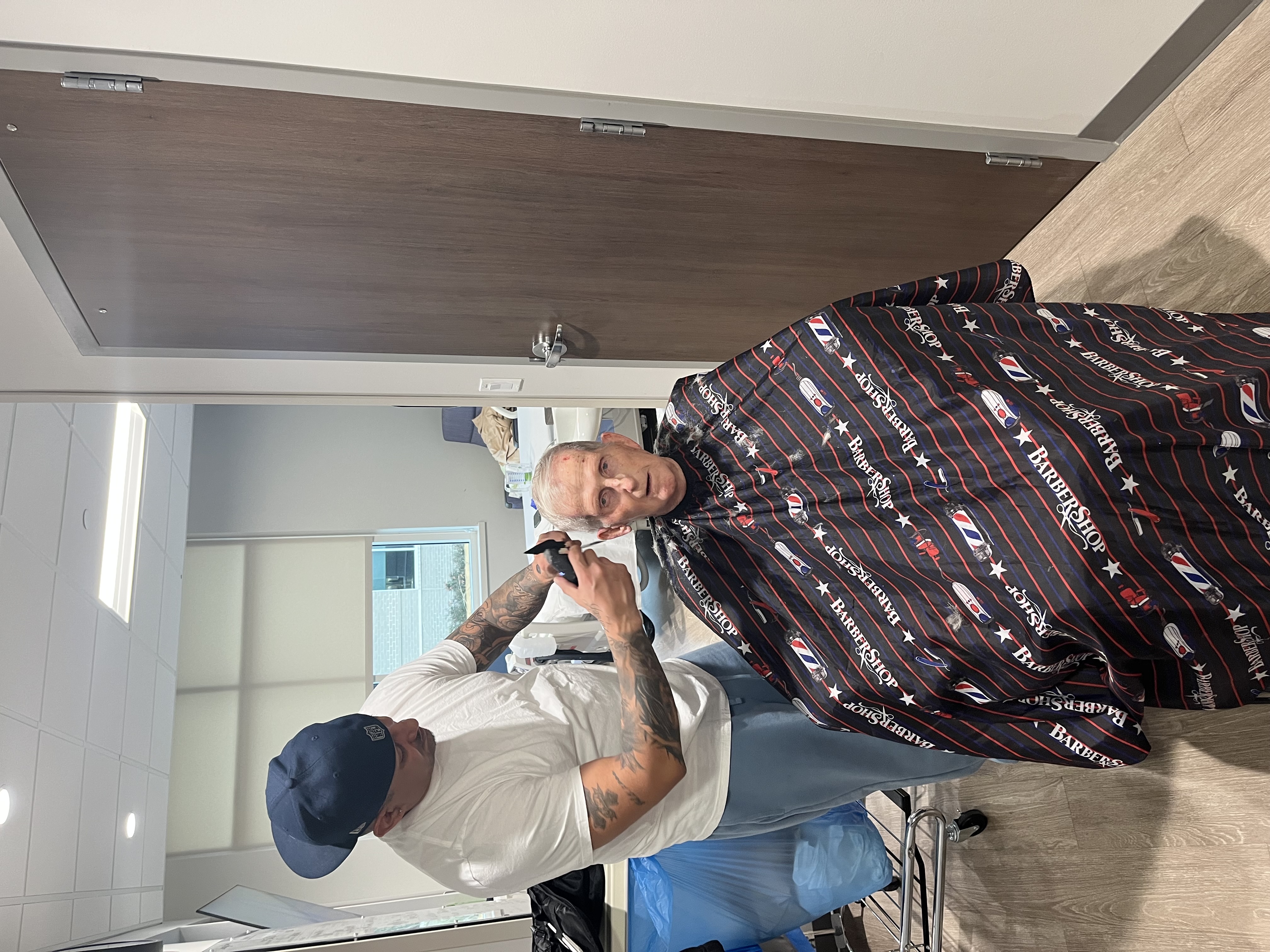 John Tepera receiving a haircut from a barber in a hospital room