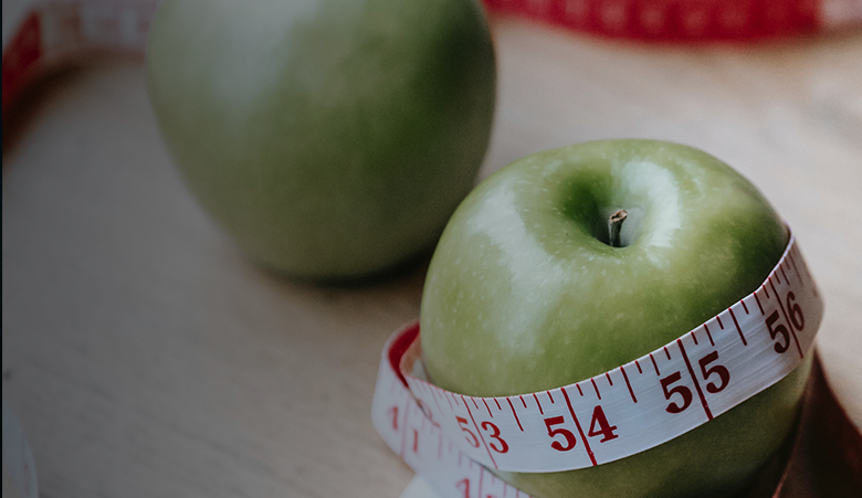 Two green apples, one with a tape measure wrapped around it.