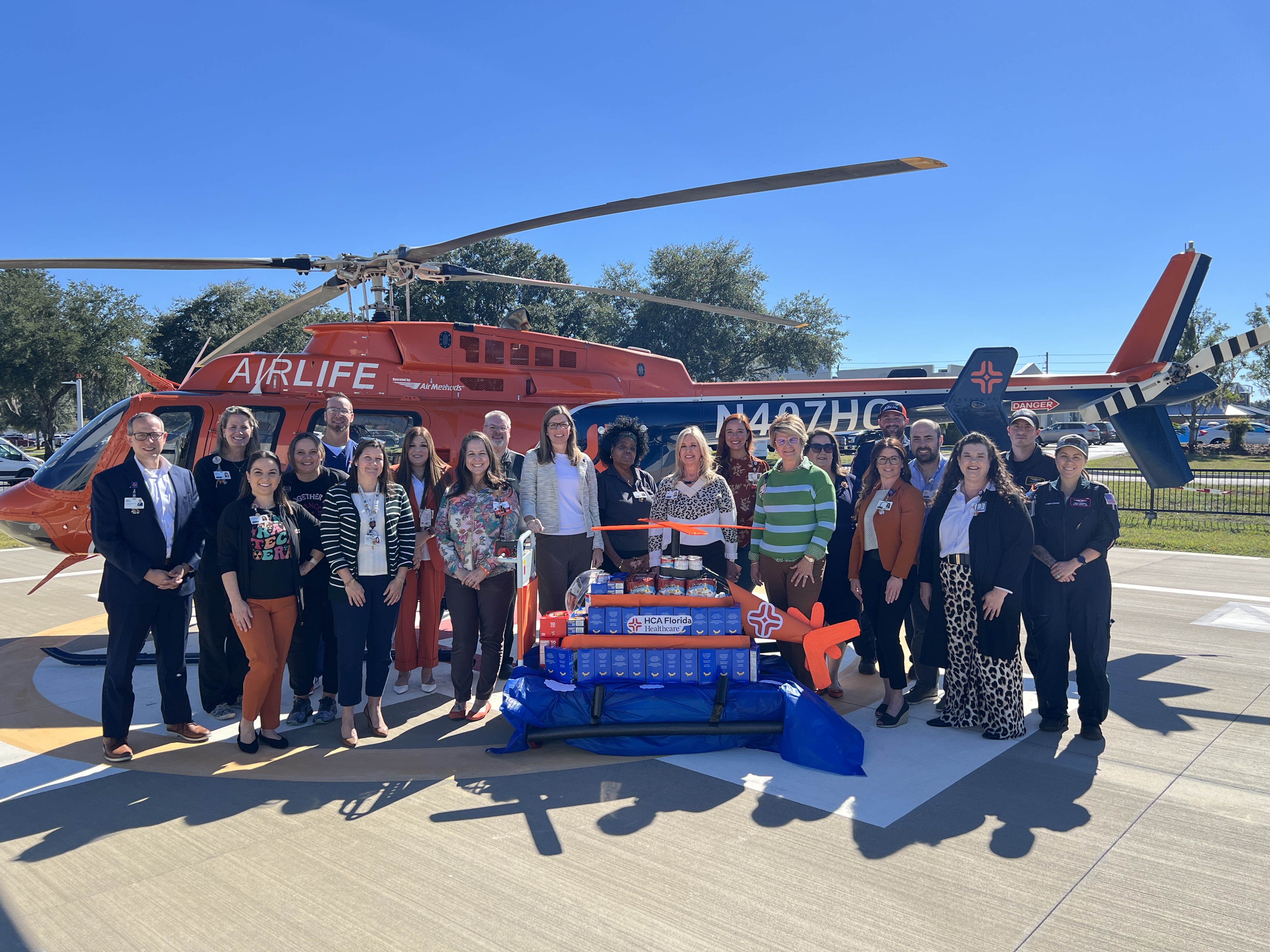A large group of people standing in front of a helicopter with a helicopter food structure positioned in front of them.