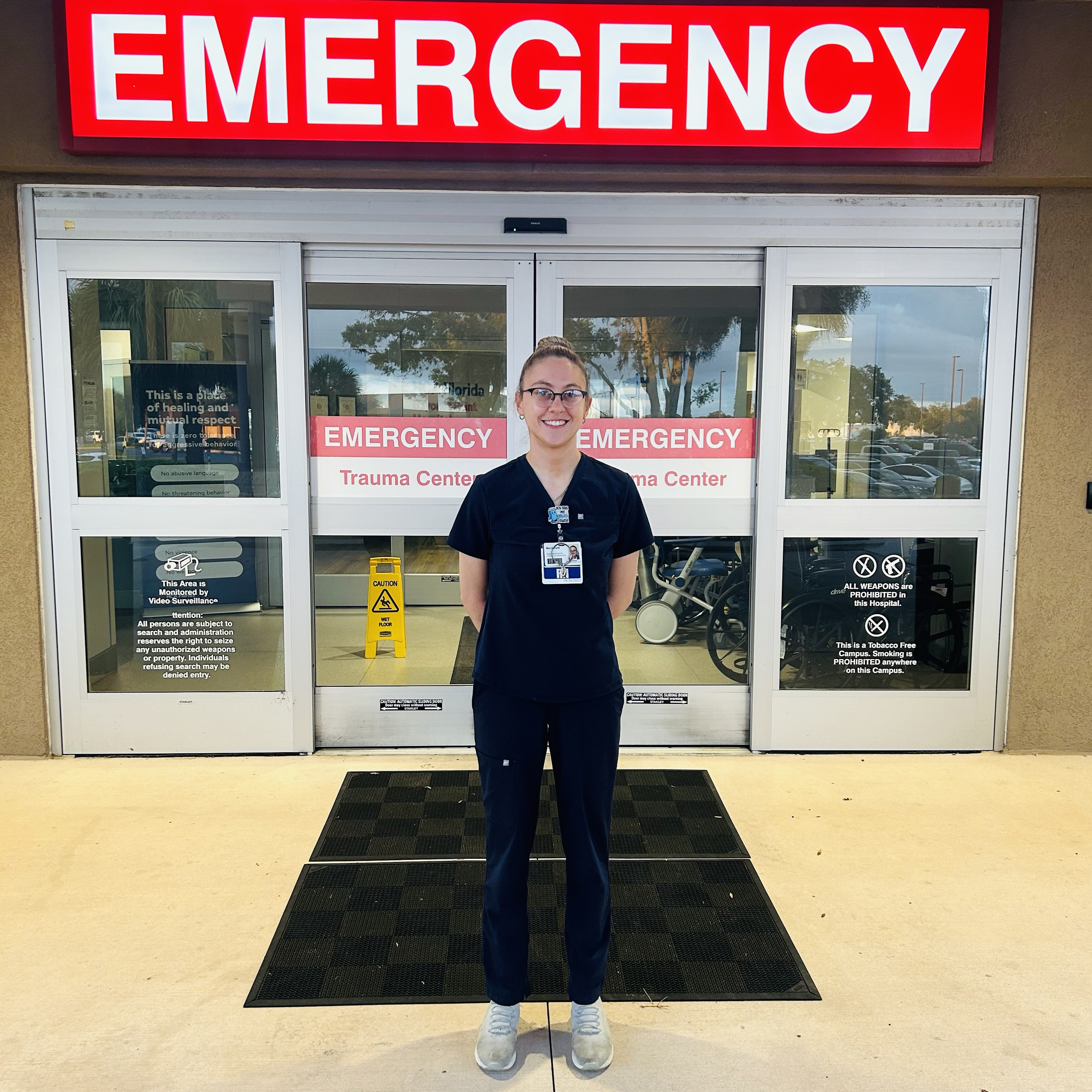 Mackenzie Beisner in work scrubs standing outside the entrance of Bayonet Hospital emergency.