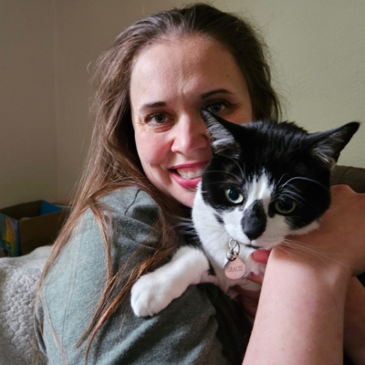 Woman smiling while holding a black-and-white cat indoors.