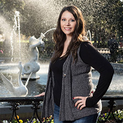 Brandy Williams smiles while standing next to an outdoor fountain.
