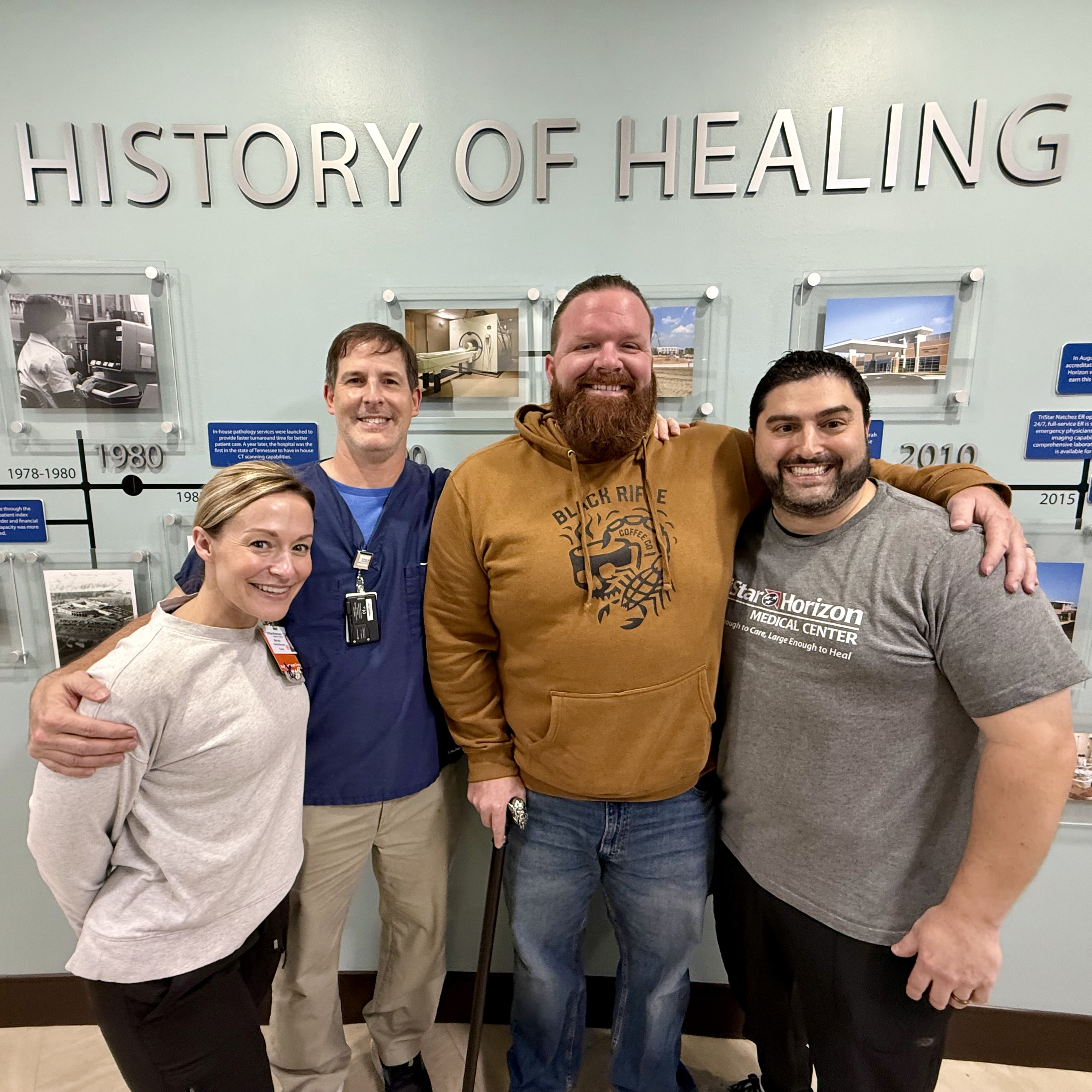Dean smiling with hospital team in front of sign that reads 'A History of Healing.'