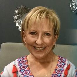 Kim Poulton smiles while wearing a colorful geometric design blouse and a gold necklace.