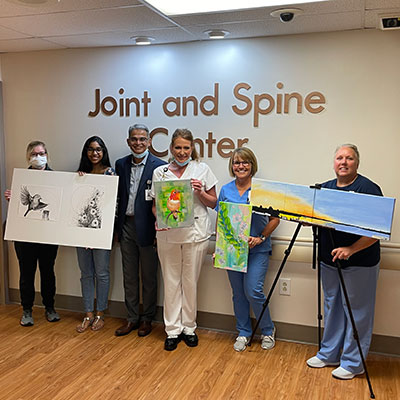 Anika Kalluri stands with her father, Dr. Prakasam Kalluri and TriCities Hospital staff, as they hold up canvas of her artwork inside the Joint and Spine Center.