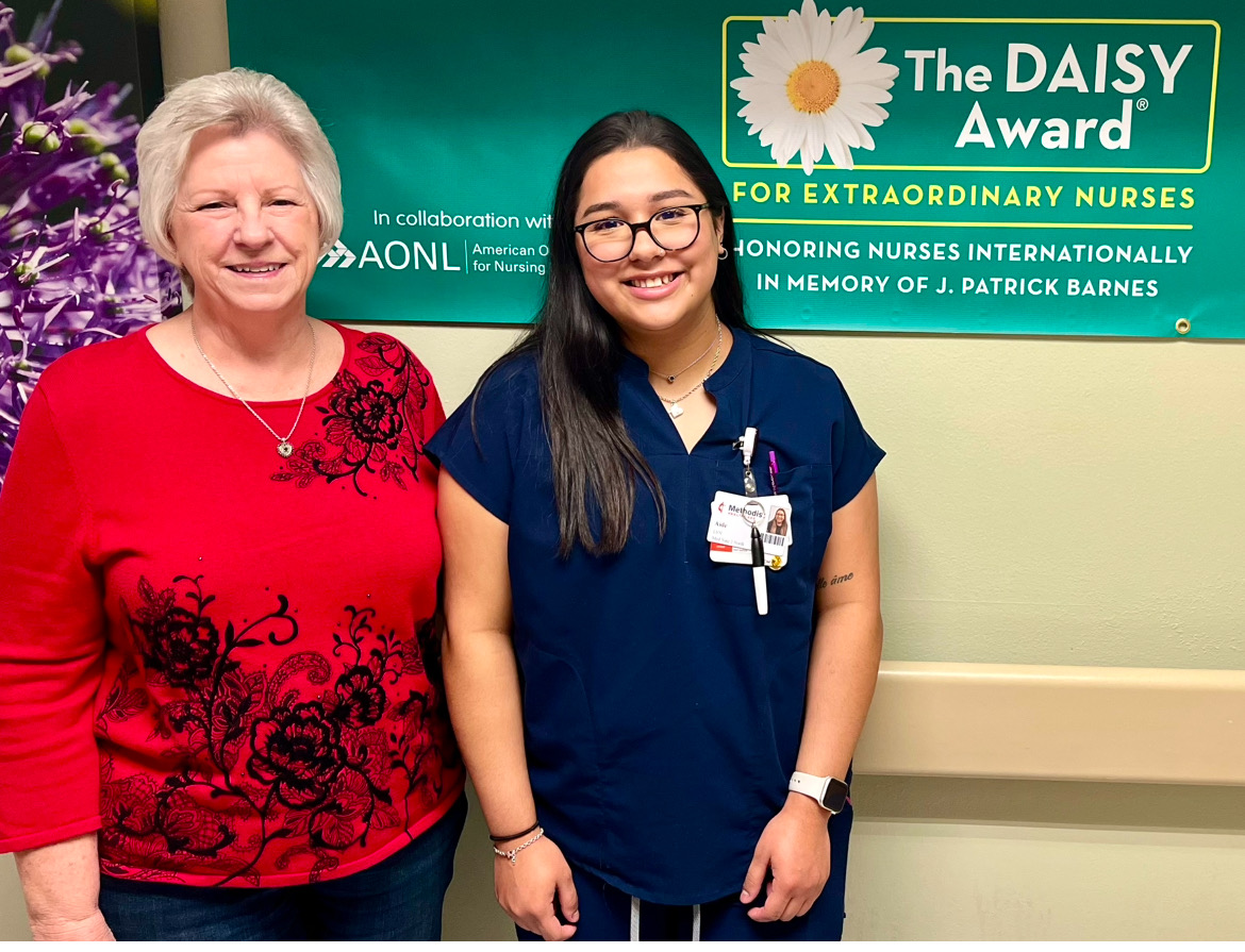 Aide Cisneros and other standing in front of sign reading- The DAISY Award for extraordinary nurses.