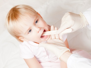 A young child opening her mouth to have her tonsils checked by a doctor.