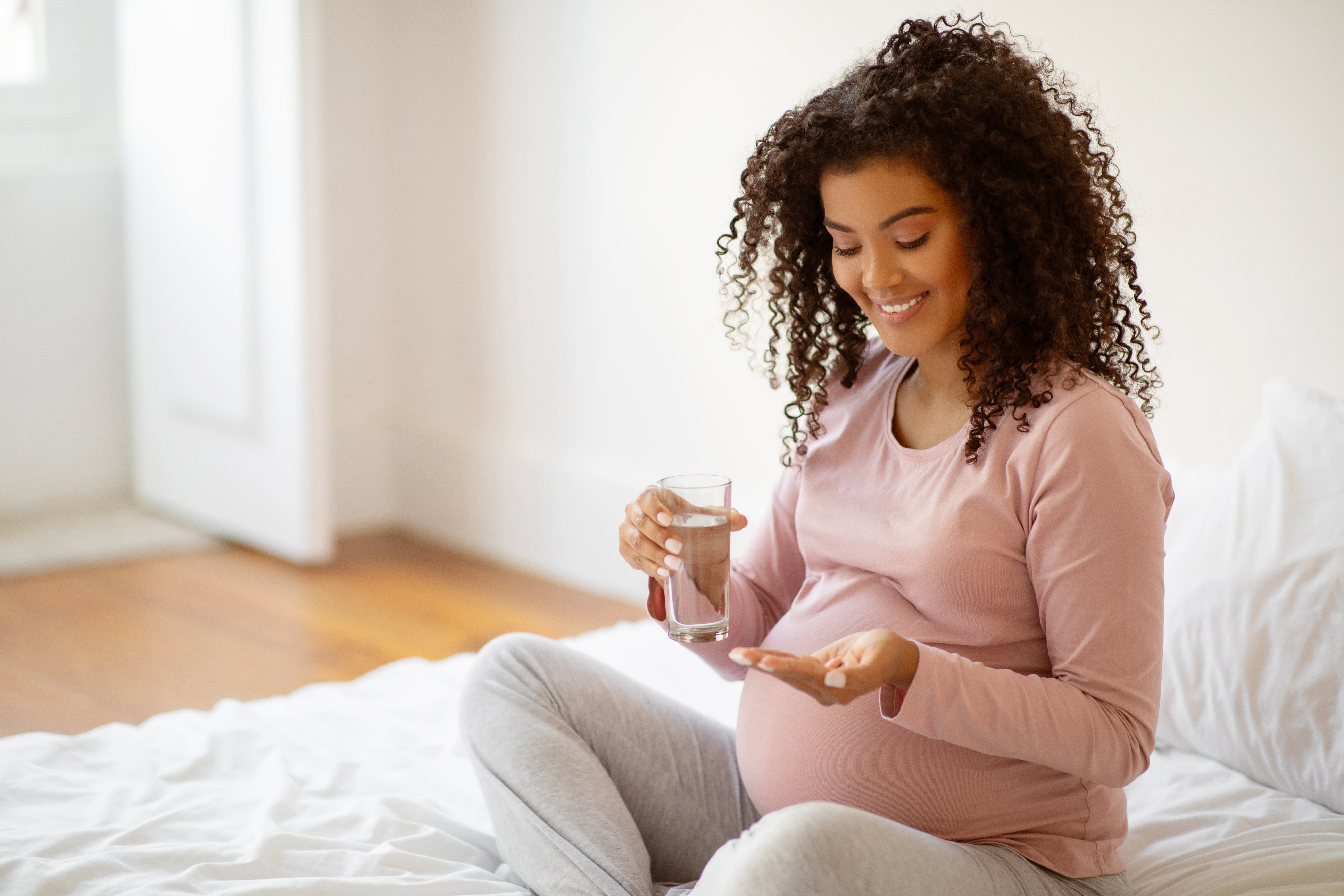 Pregnant woman in pink shirt holding glass of water and holding pills in an open hand.
