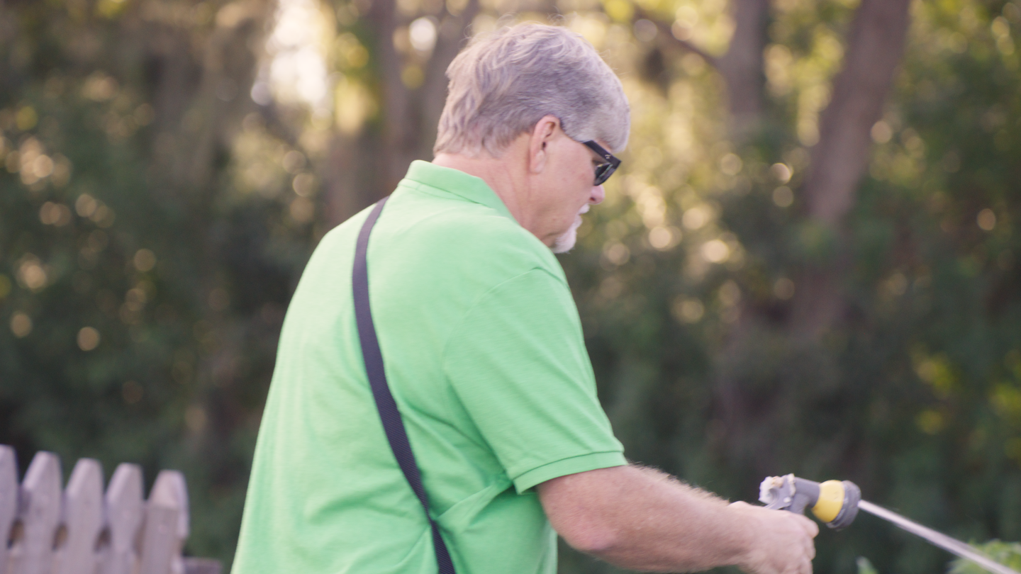 Jeff Pollier watering plants with a garden hose.
