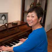 Cancer survivor Claribel Dare looks over her shoulder and smiles while playing a piano. 