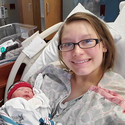 Courtney Hathaway smiling with her swaddled newborn baby boy in her arms, in her hospital bed.