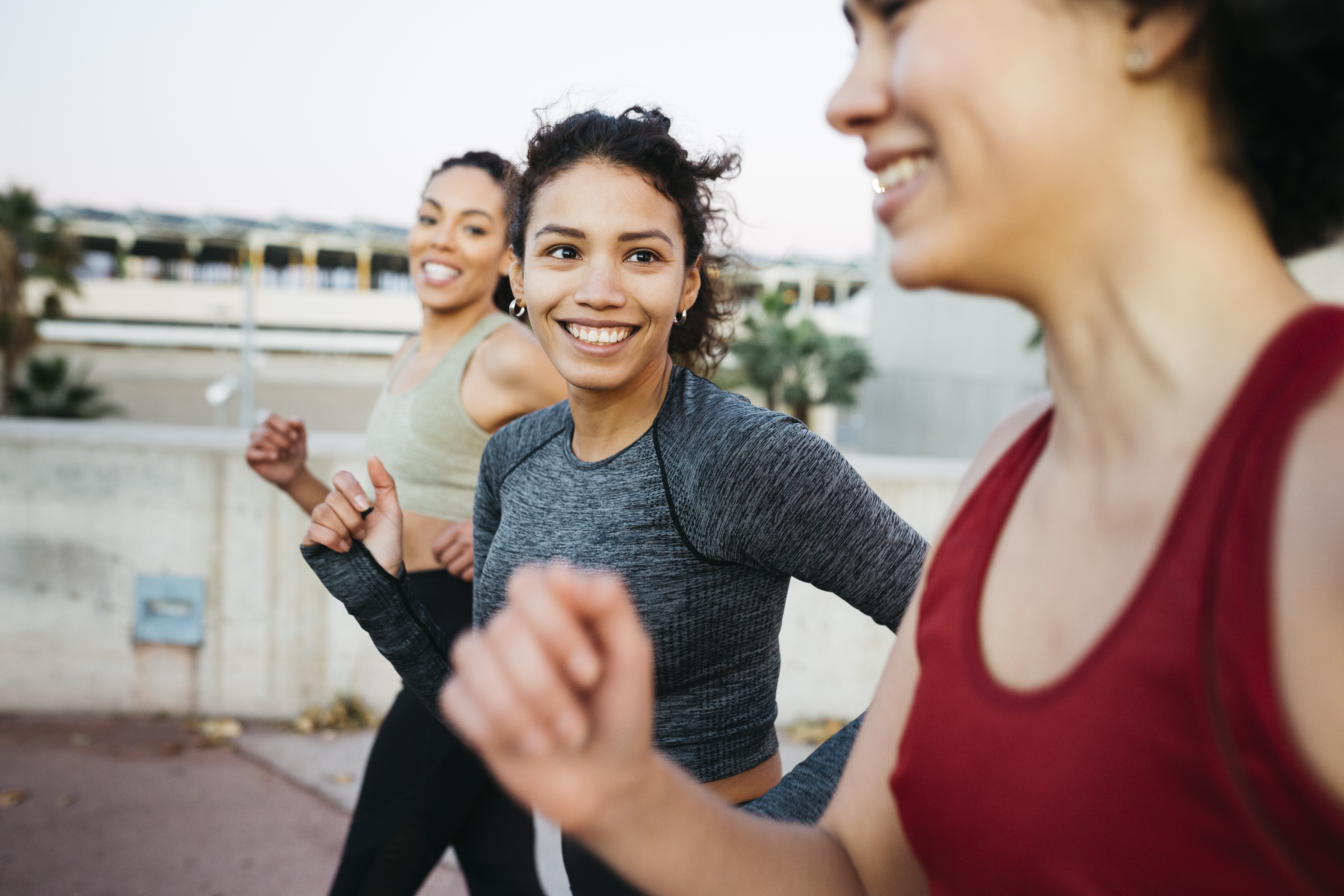 Three young women wearing fitness attire smile while jogging outdoors.