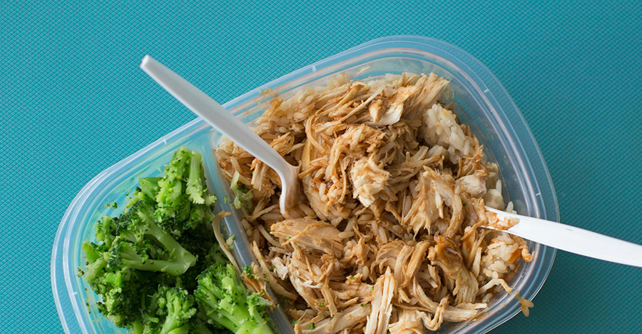 A plastic container with chicken and broccoli inside.