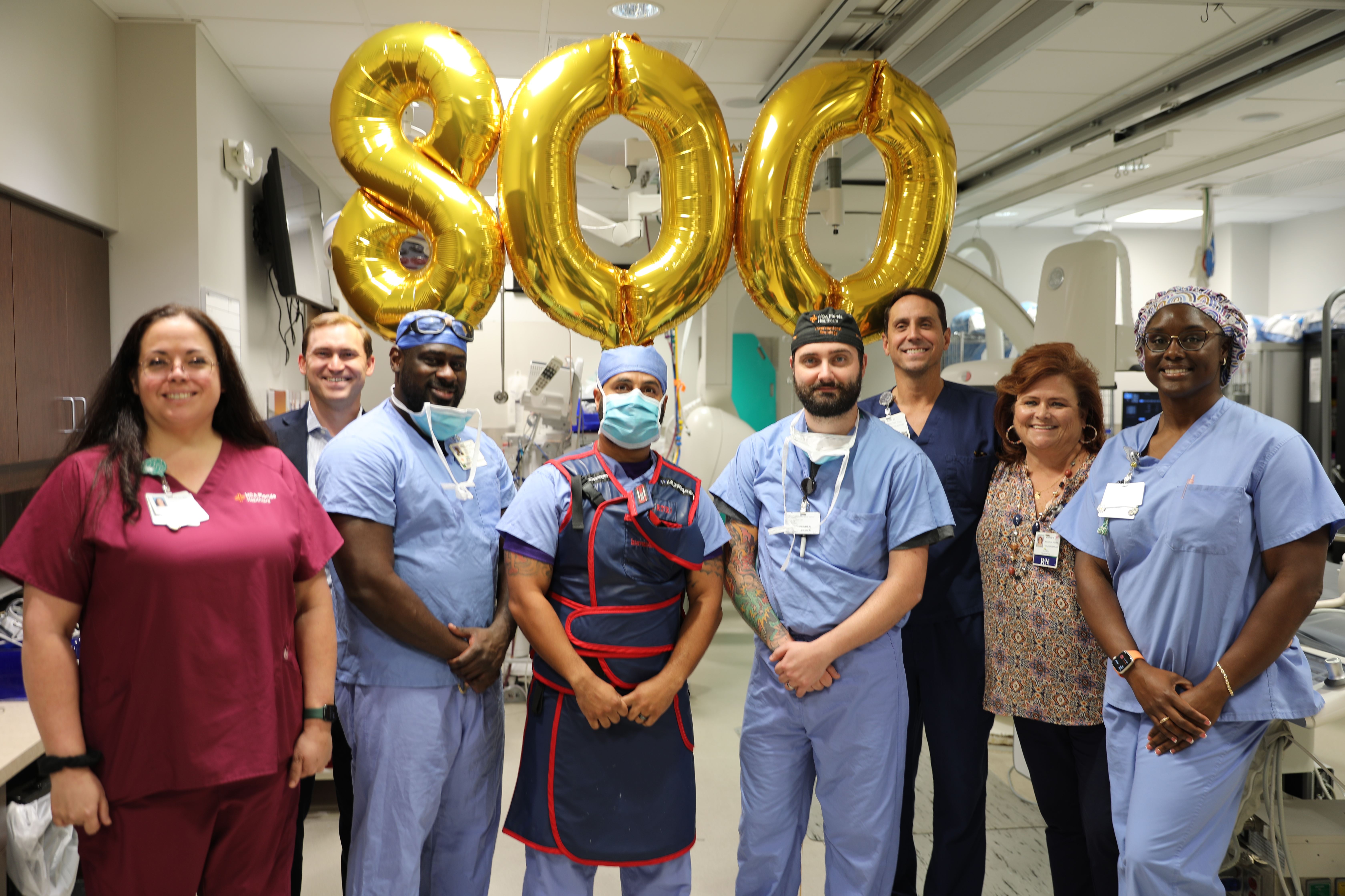 group of people standing in hospital cardiology unit with gold balloons that spell out "800"
