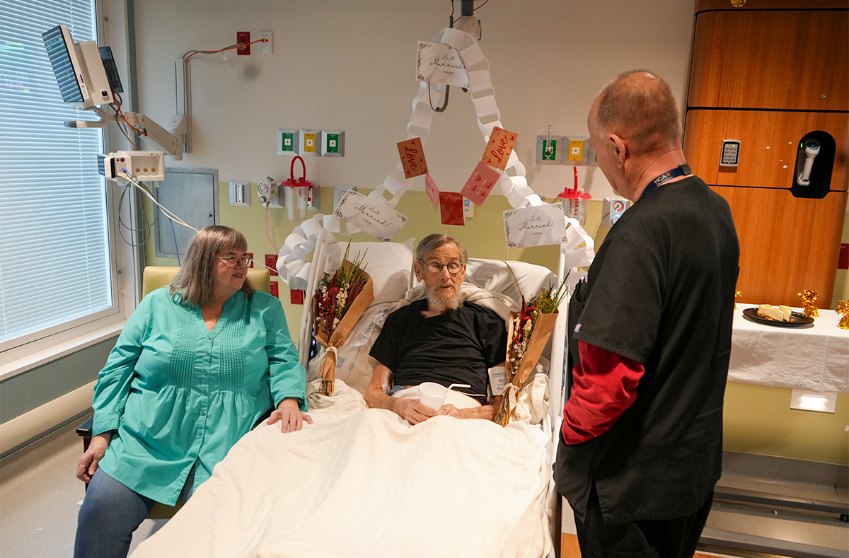 Marlene sits on William's hospital bed as they speak with Centennial team member.