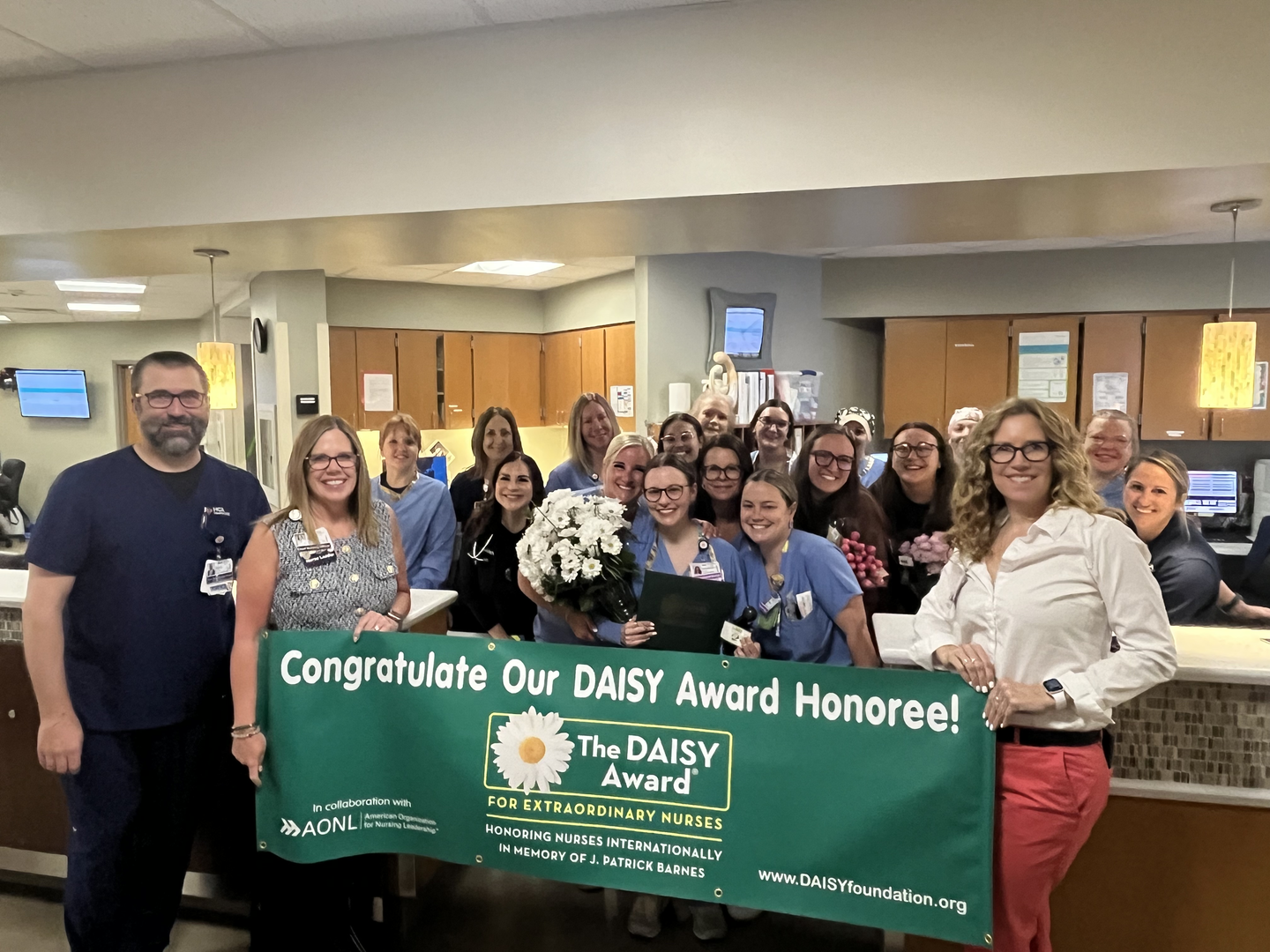 Paige Payshence and her team smiling and posing for a photo, while holding the daisy award banner.